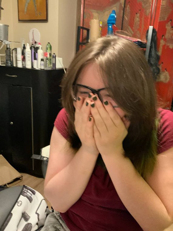 A client covering her face in delight after her colour at Shear Lady Salon LLC, green ends through long brown hair